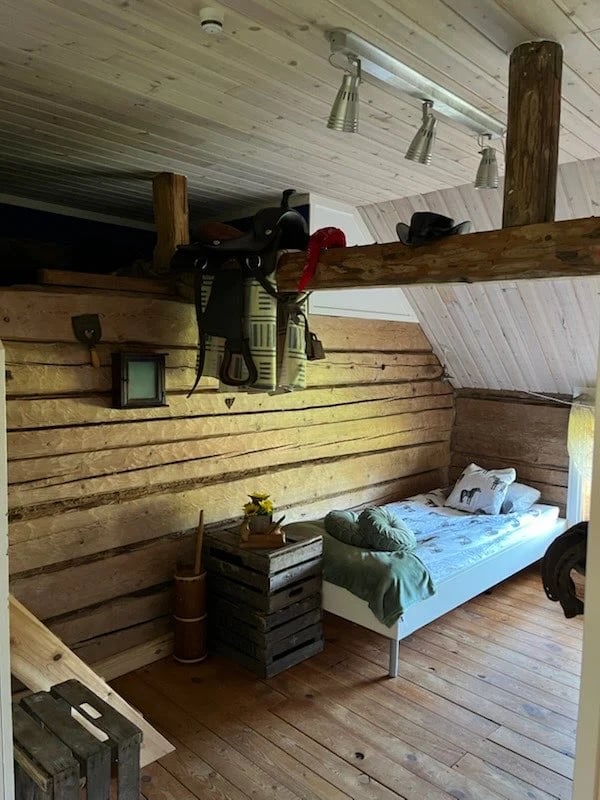 Interior of rustic wooden cabin bedroom with bed, exposed beam ceiling, and tools mounted on wall